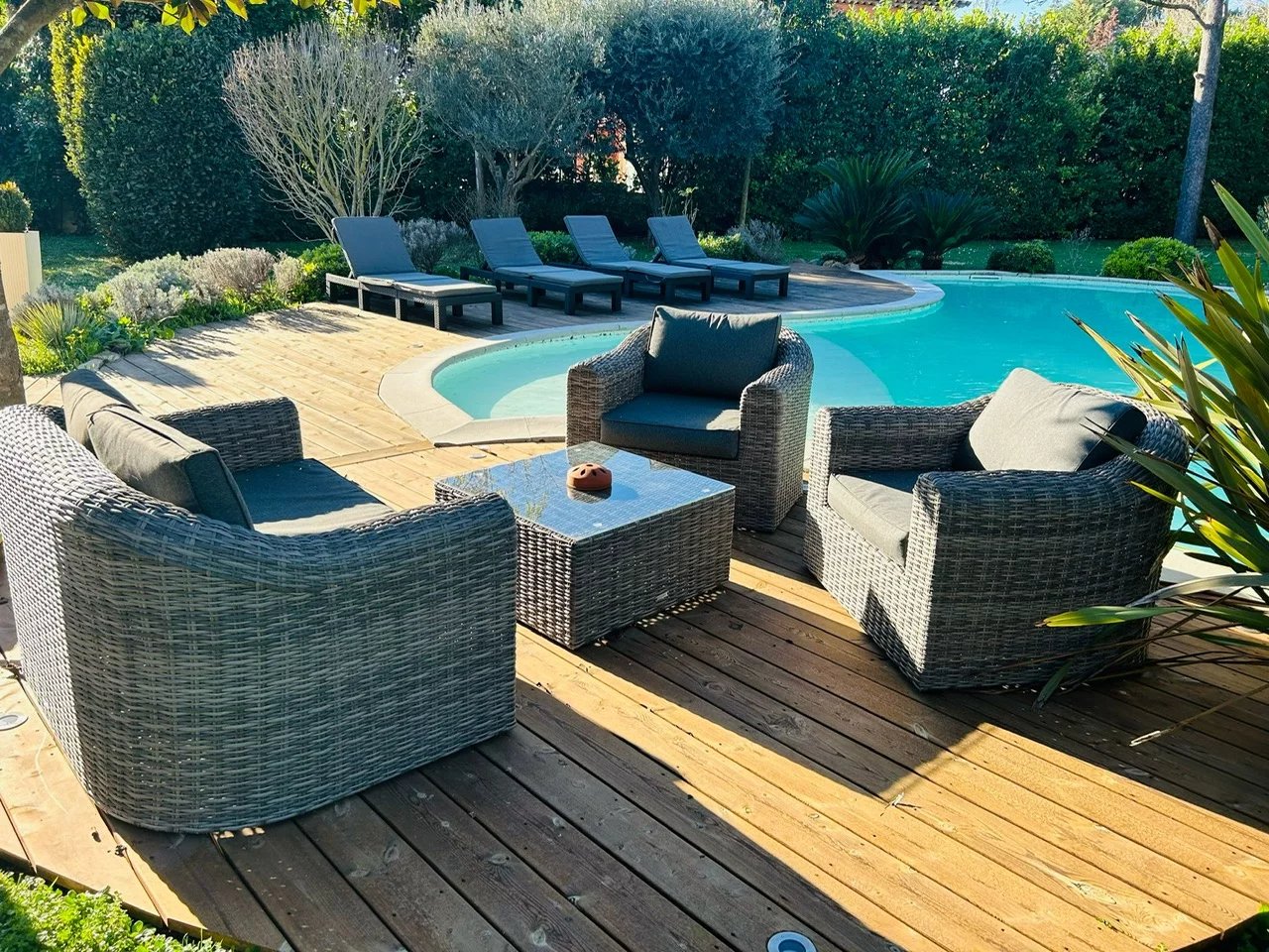 Espace extérieur d'une villa avec piscine, chaises longues et salon de jardin en rotin sur une terrasse en bois.