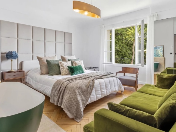 Chambre d'un appartement à Cannes avec lit, fauteuils verts et baignoire.