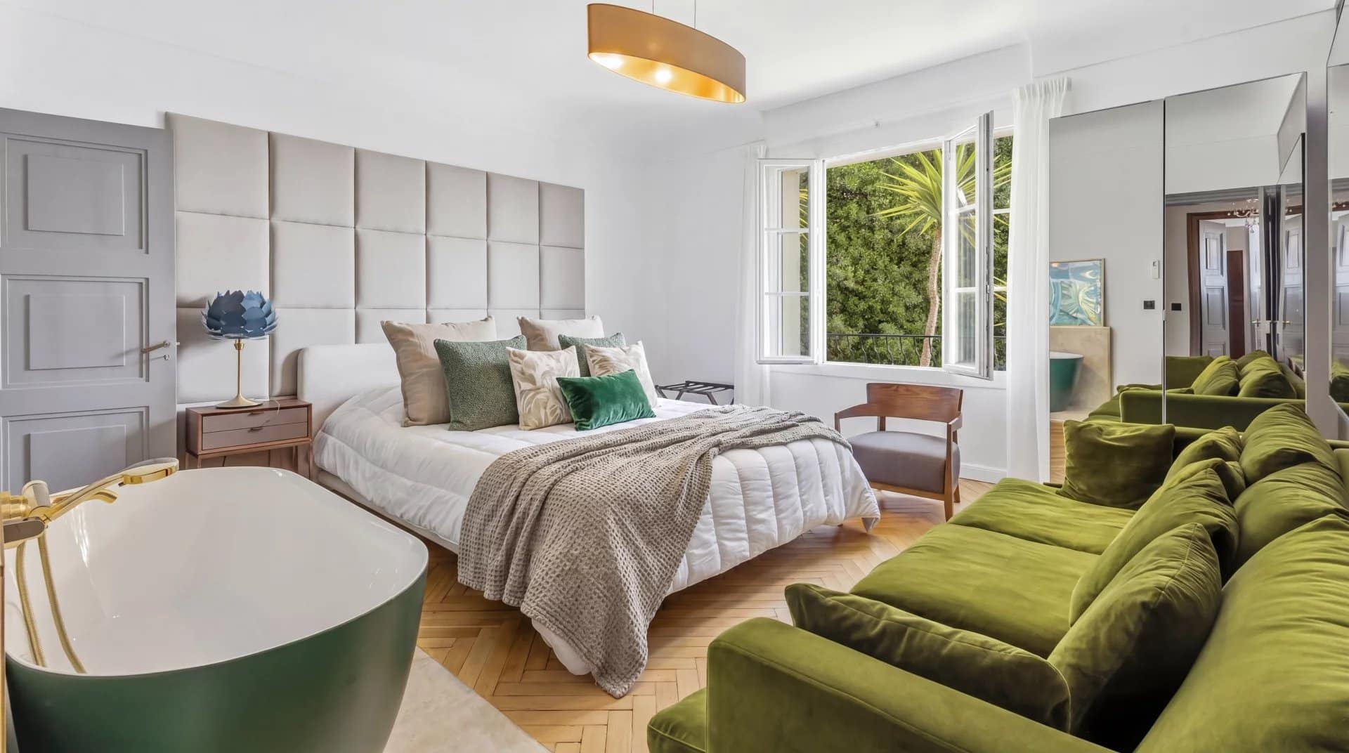 Chambre d'un appartement à Cannes avec lit, fauteuils verts et baignoire.