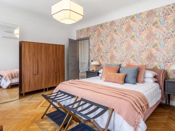 Chambre élégante avec un lit double, des meubles en bois et un mur décoré de motifs floraux.