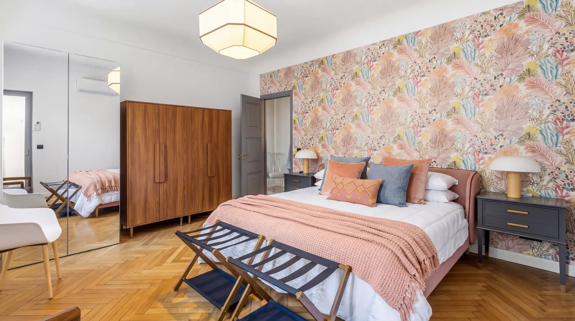 Chambre élégante avec un lit double, des meubles en bois et un mur décoré de motifs floraux.