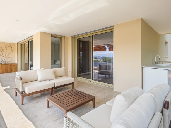 Terrasse couverte d'un appartement avec mobilier moderne et cuisine d'été, vue sur mer et collines.