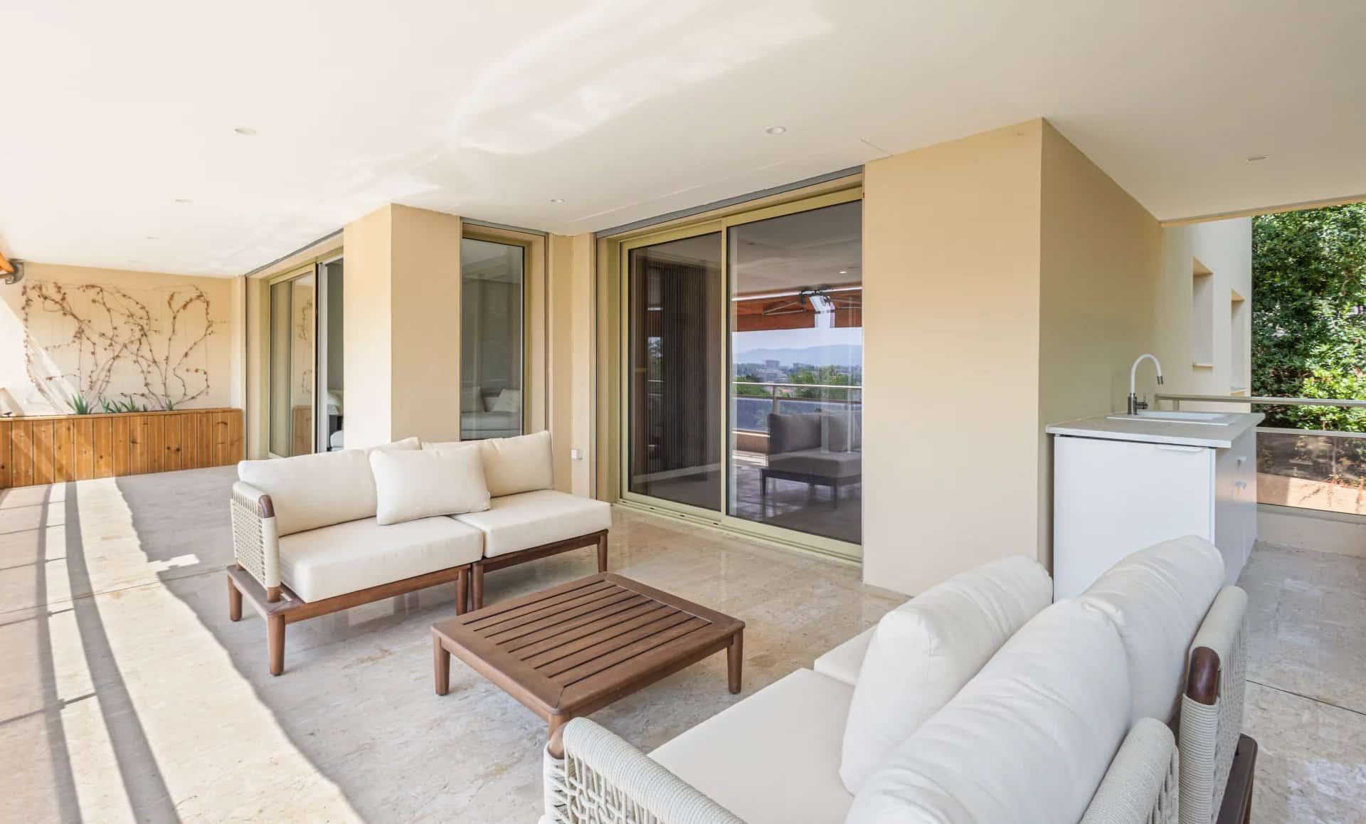 Terrasse couverte d'un appartement avec mobilier moderne et cuisine d'été, vue sur mer et collines.