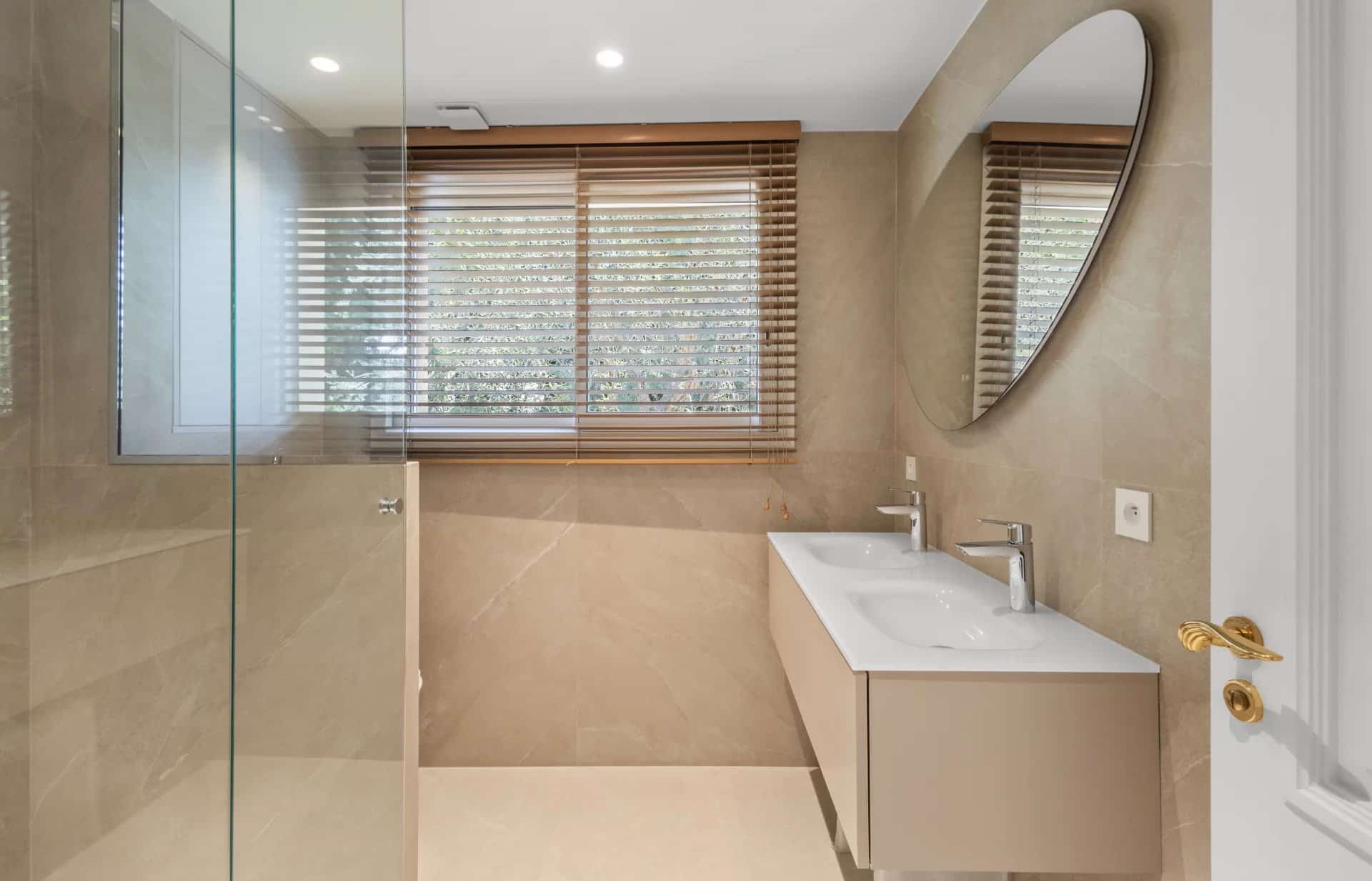Salle de bain moderne avec douche en verre et double vasque, éclairage naturel.