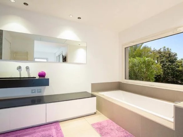 Modern bathroom with bathtub, mirror and garden view.
