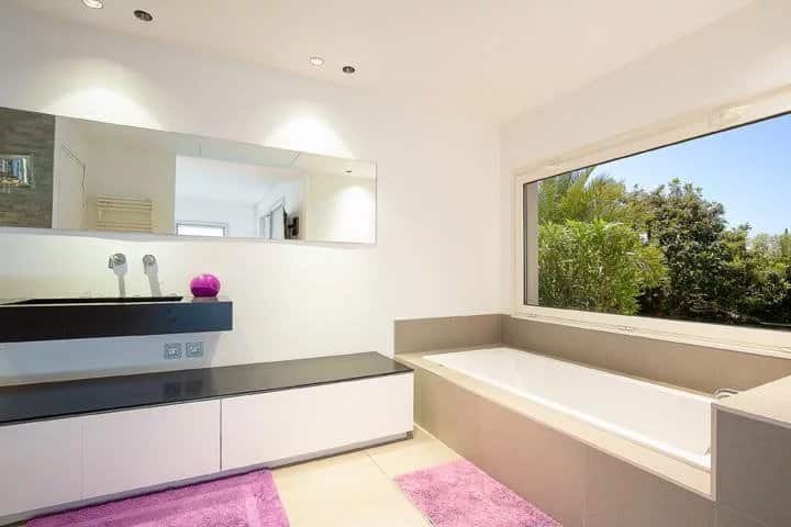 Modern bathroom with bathtub, mirror and garden view.