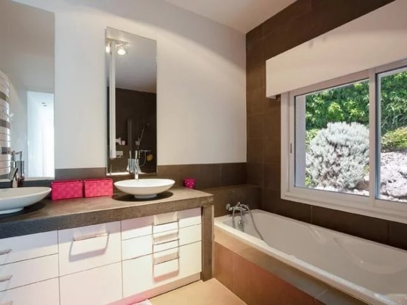Modern bathroom with bathtub and sink, window overlooking a garden.