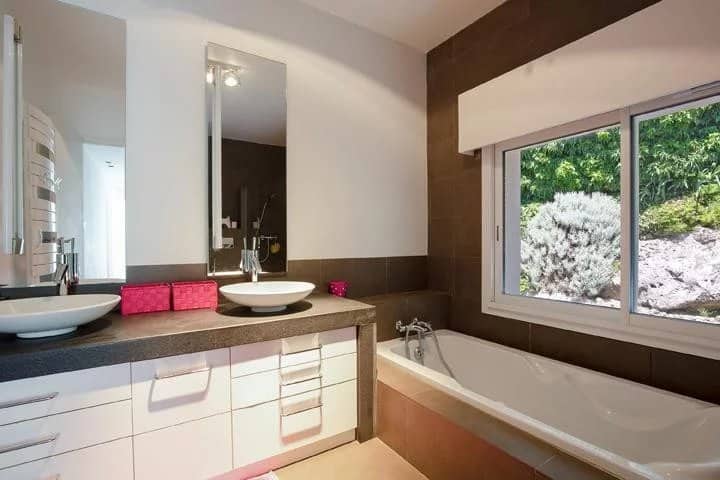 Modern bathroom with bathtub and sink, window overlooking a garden.