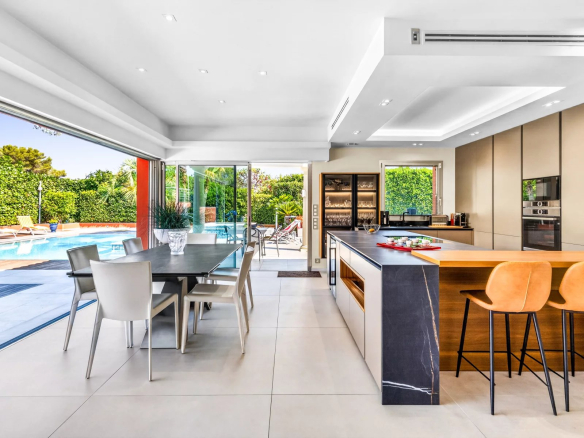 Intérieur d'une villa moderne avec cuisine équipée et salle à manger, vue sur la piscine extérieure.