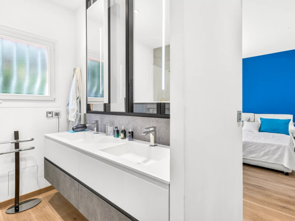 Salle de bain moderne avec double vasque et miroir, chambre à coucher en arrière-plan.