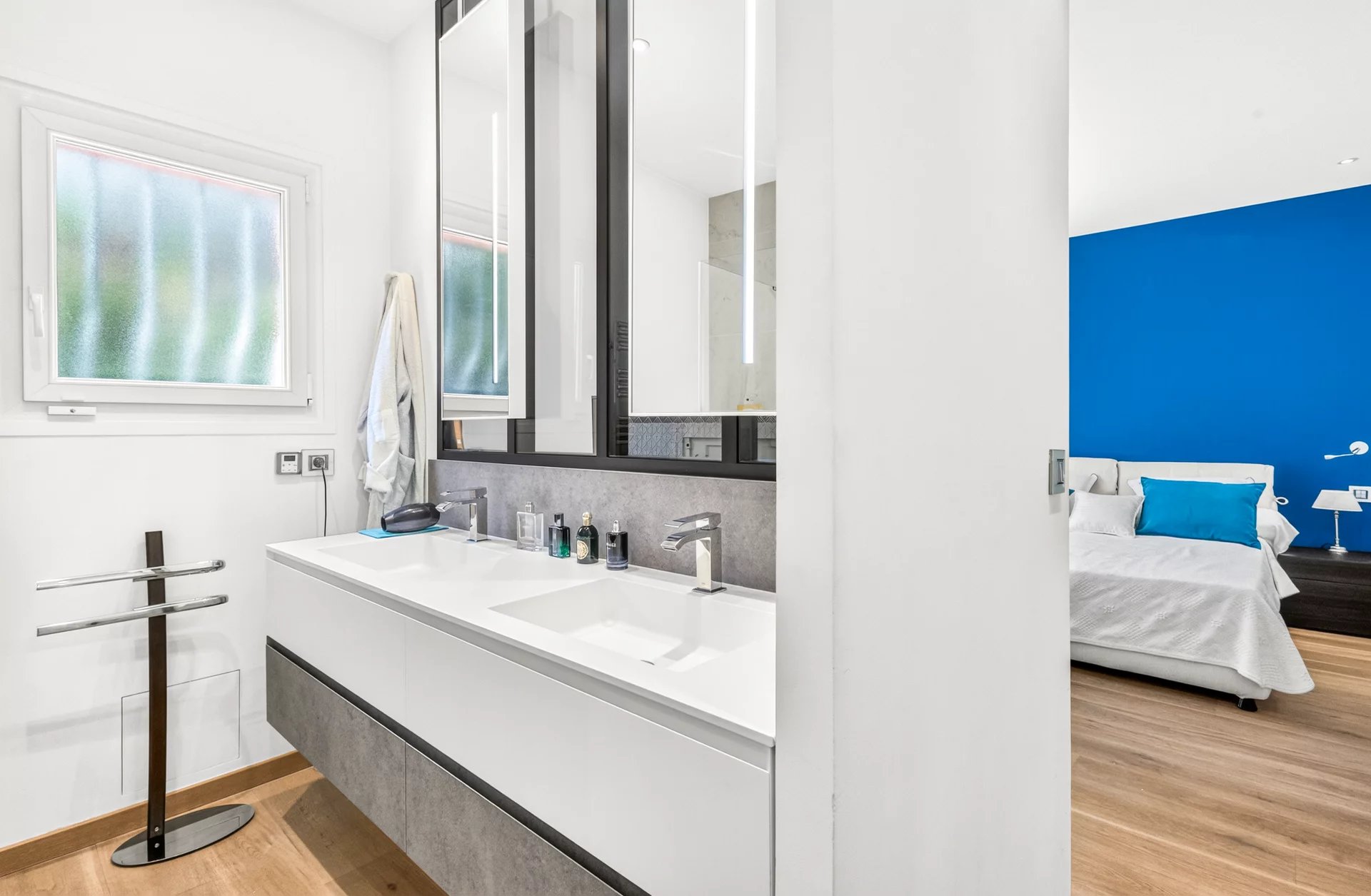 Salle de bain moderne de la villa à Mougins Salle de bain moderne avec double vasque et miroir, chambre à coucher en arrière-plan.
