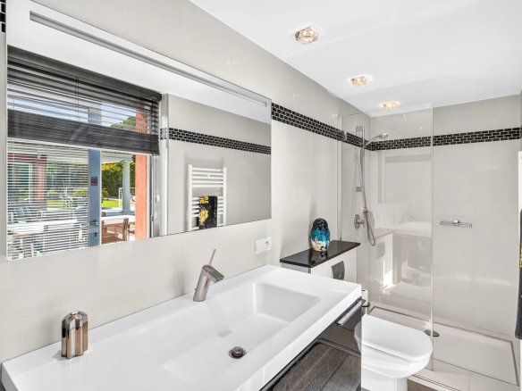 Salle de bain moderne avec douche et lavabo, vue sur l'extérieur avec piscine
