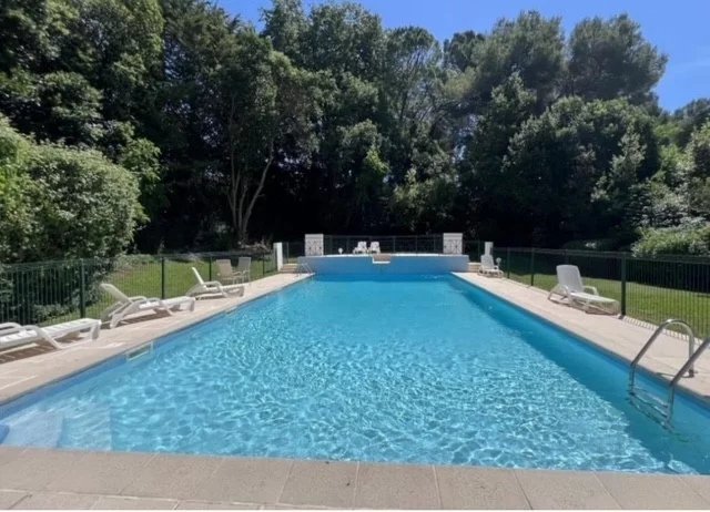 Swimming pool in a gated community in Cannes, surrounded by greenery and sun loungers.