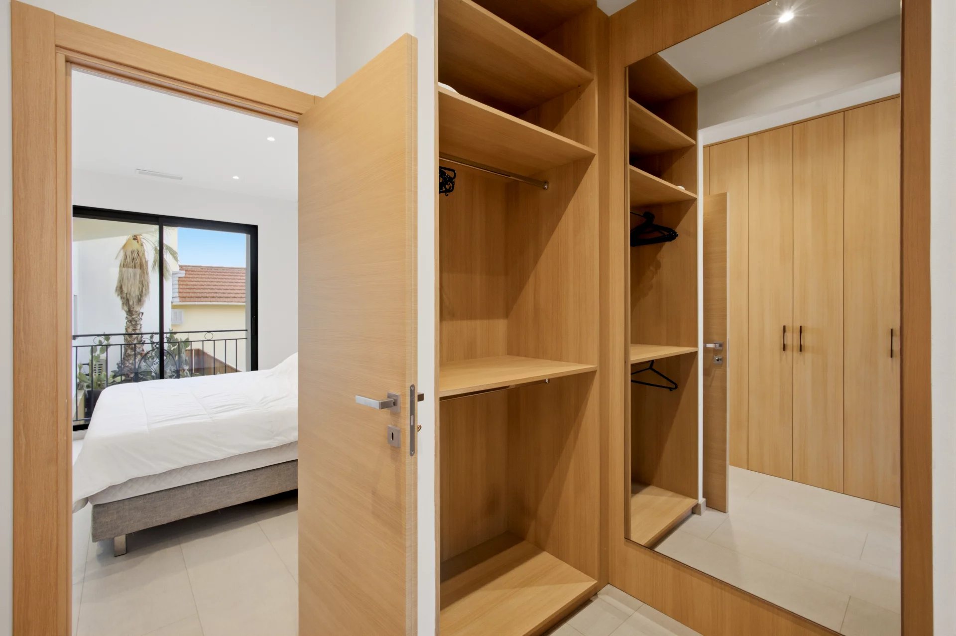 Bedroom with wardrobe and mirror Interior of a bedroom with a wooden wardrobe and mirror, overlooking a bed and a terrace.