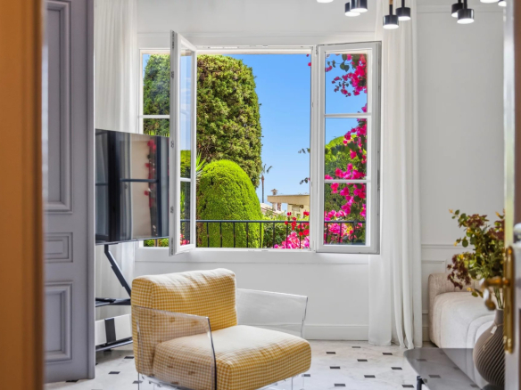 Vue intérieure d'un appartement à Cannes avec fenêtres ouvertes sur un jardin fleuri.