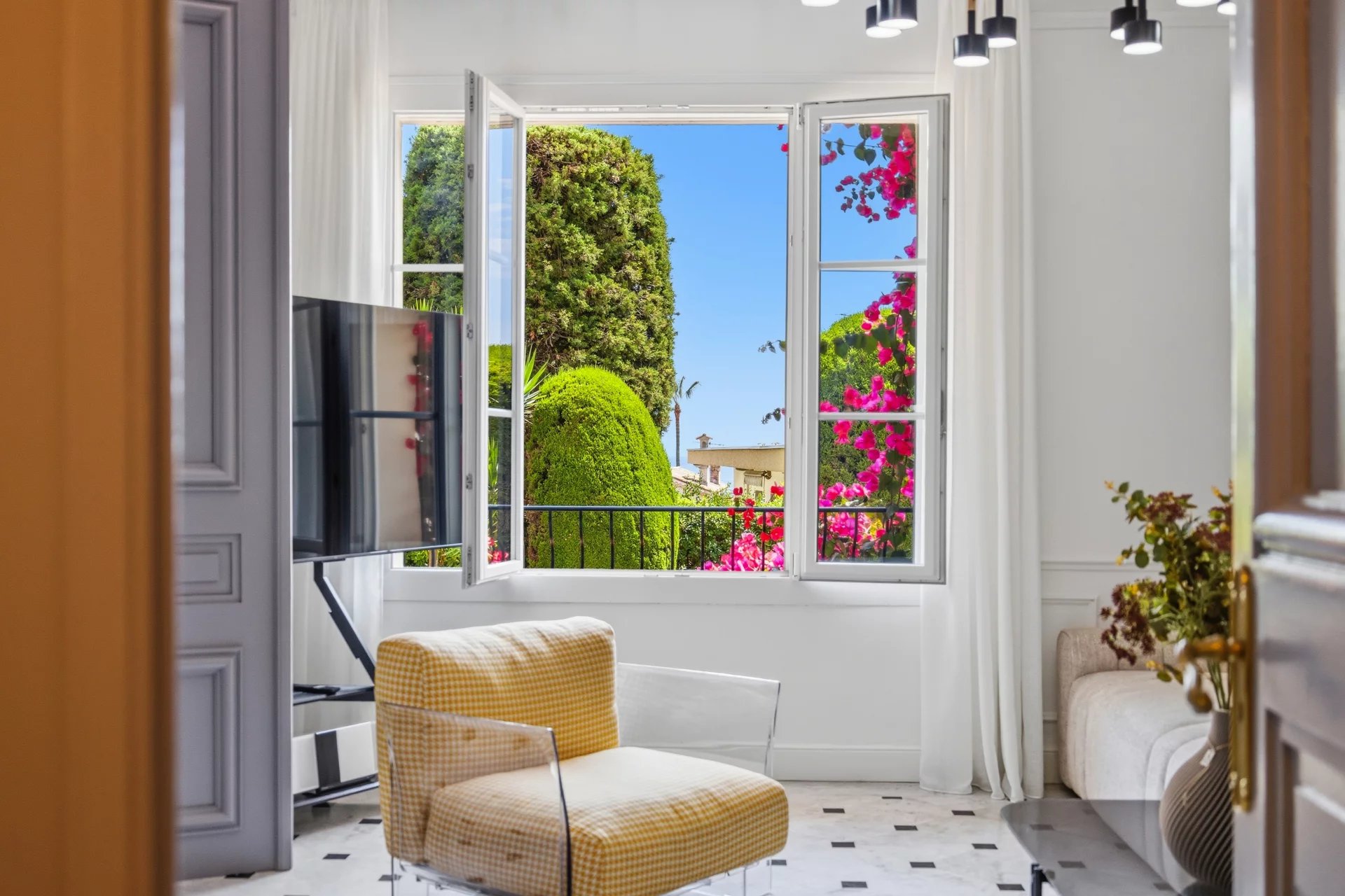 Appartement à Cannes avec vue sur jardin Vue intérieure d'un appartement à Cannes avec fenêtres ouvertes sur un jardin fleuri.