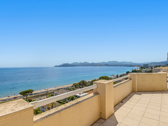 Vue panoramique sur la mer depuis une terrasse à Cannes, avec des montagnes en arrière-plan.