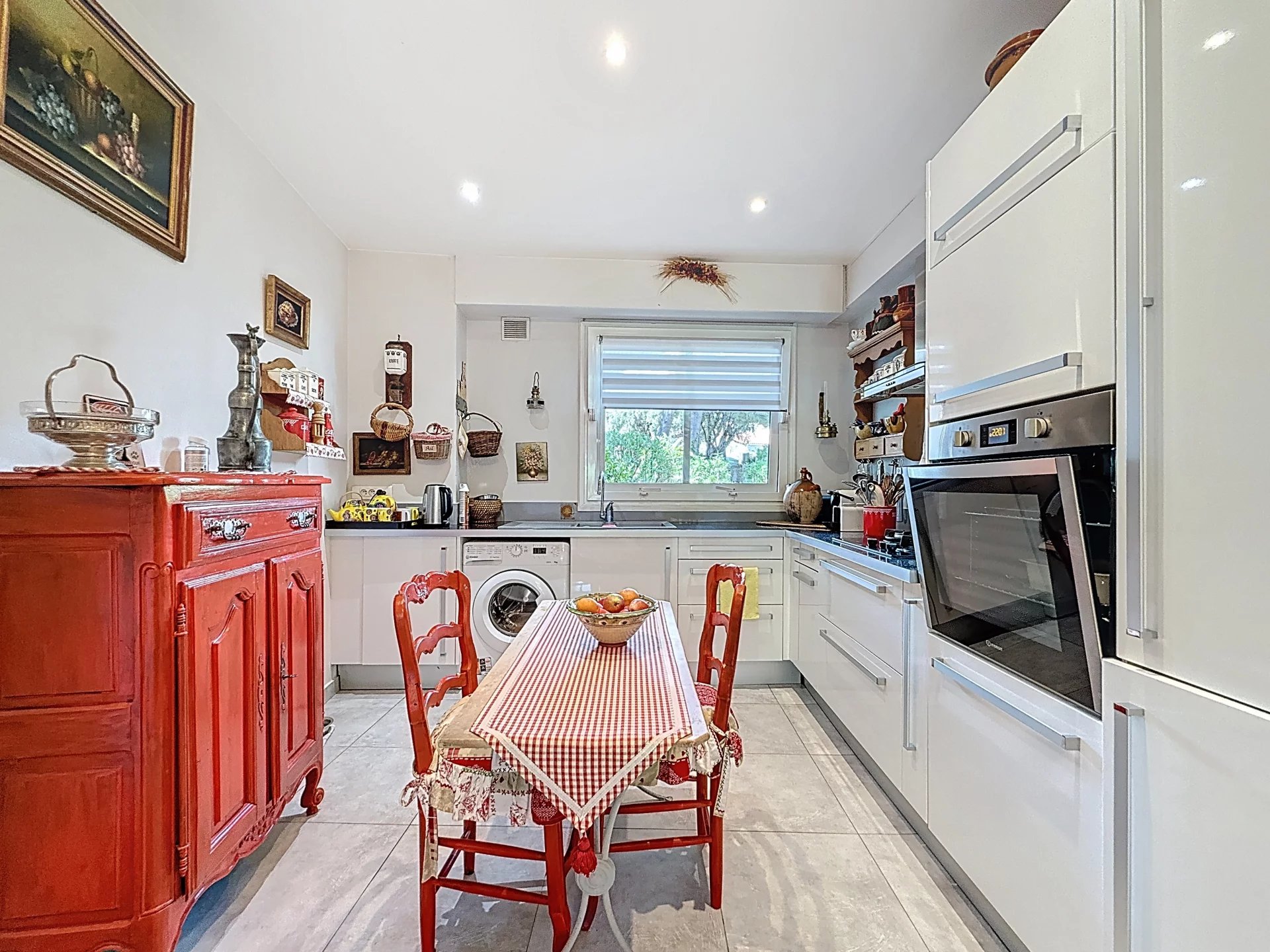 Cuisine rénovée avec table à manger Cuisine moderne avec mobilier rouge et table à manger, éclairée par la lumière naturelle.