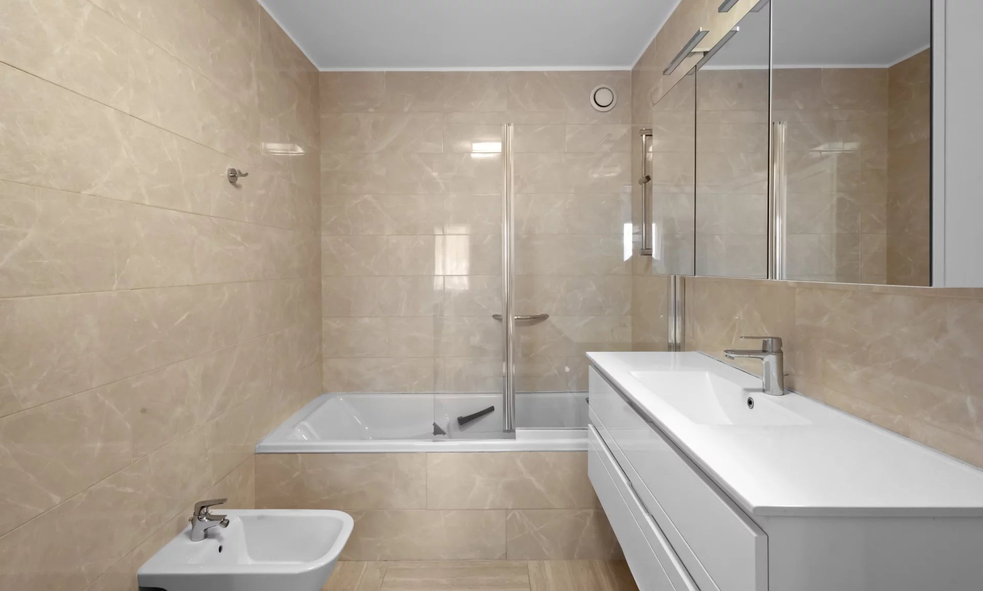 Bathroom of an apartment in Le Cannet Modern bathroom with bathtub and shower, beige tiles.