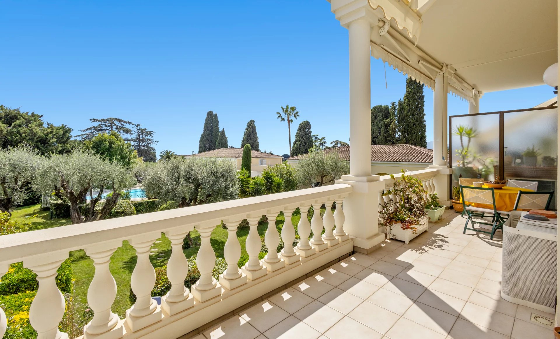Balcon d'un appartement à Cannes avec vue sur jardin et piscine, ensoleillé.