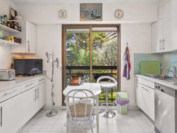 Cuisine lumineuse avec vue sur un jardin, équipée de meubles blancs et d'une table pour deux.