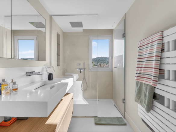 Salle de bain moderne avec douche, lavabo et miroir, vue sur la colline à travers la fenêtre.