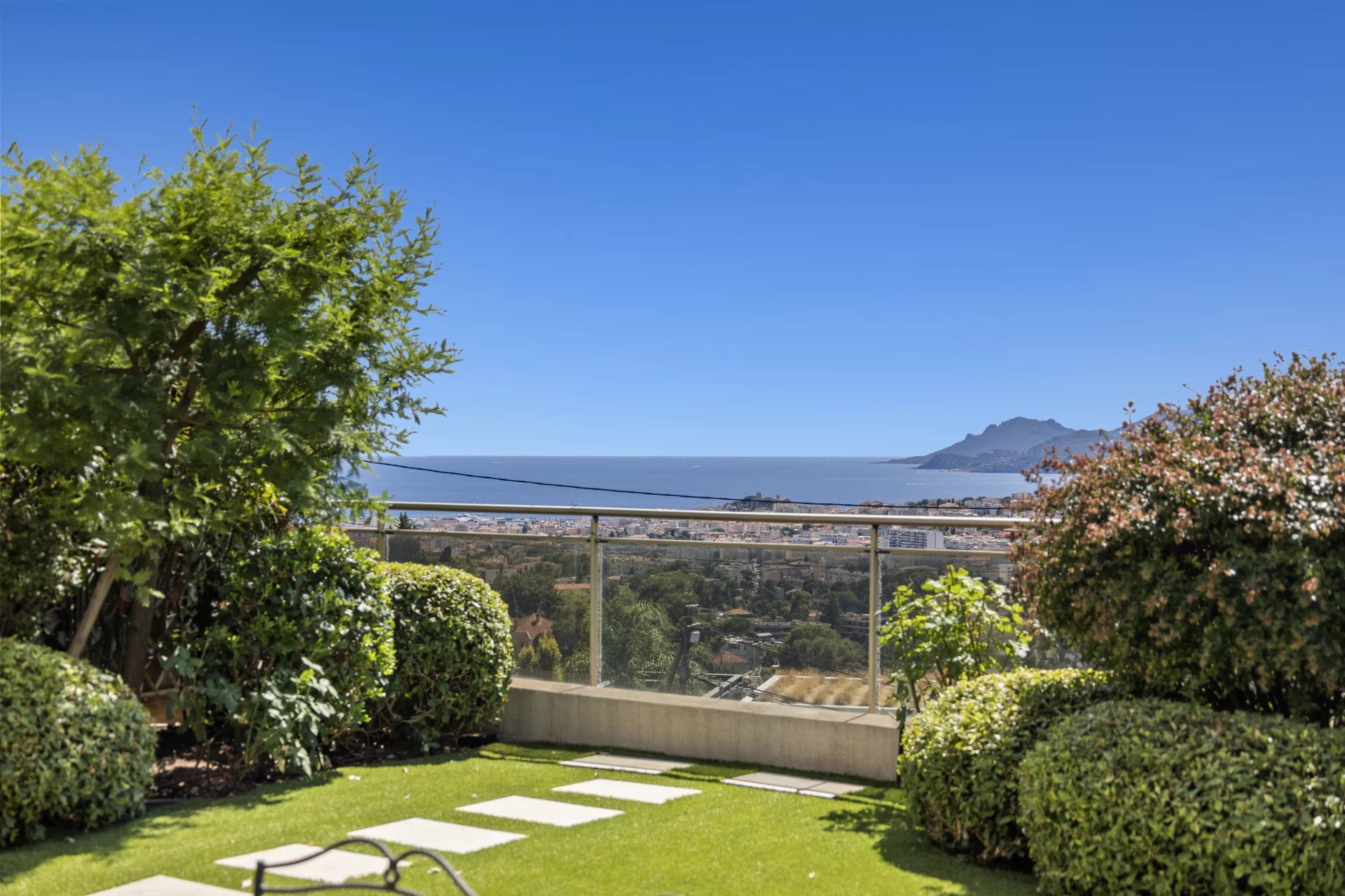 Vue panoramique sur la mer depuis une terrasse avec jardin, entourée de verdure.