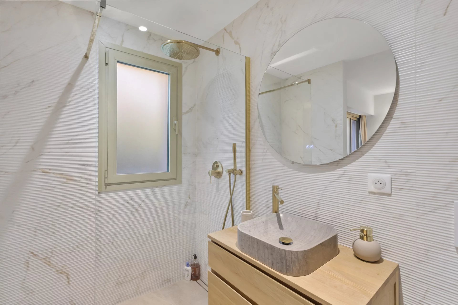 Modern bathroom in Le Cannet Modern bathroom with shower and wooden furniture, marble tiles, window and round mirror.