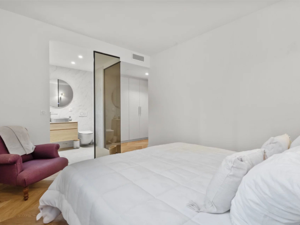Room in a renovated apartment with a bed and an armchair, overlooking a modern bathroom.