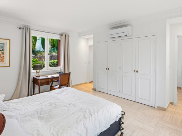 Chambre d'une villa rénovée au Cannet, avec lit, bureau et fenêtre donnant sur un jardin verdoyant.