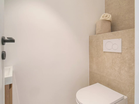 Toilettes modernes avec carrelage beige et mur blanc dans un appartement rénové.