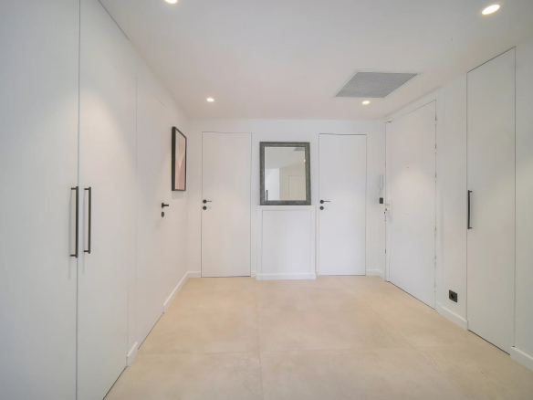 Entrée d'un appartement moderne avec murs blancs et sol en carrelage beige.