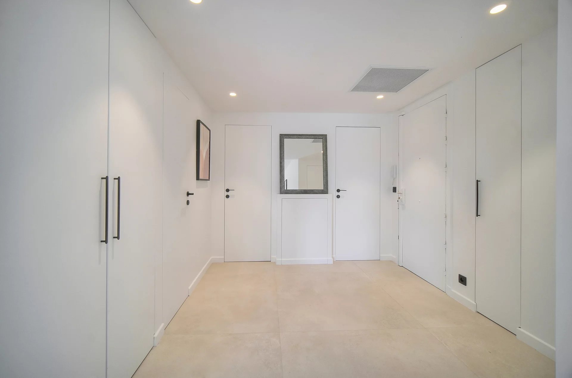 Entrée d’appartement au Cannet Europe Entrée d'un appartement moderne avec murs blancs et sol en carrelage beige.