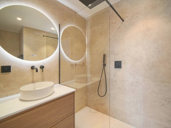 Salle de bain moderne avec douche à l'italienne et miroir rond lumineux.
