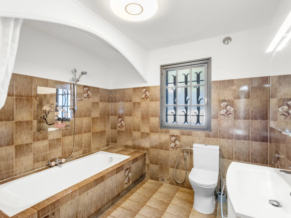 Bathroom with bathtub and toilet, brown tiles, window with bars.