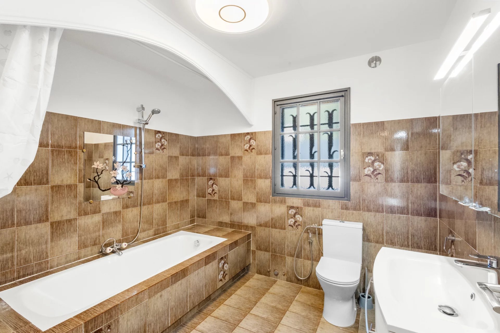 Bathroom with bathtub and toilet, brown tiles, window with bars.