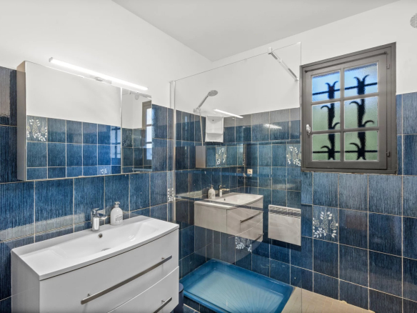 Modern bathroom with blue tiles and vanity unit, window with patterns.