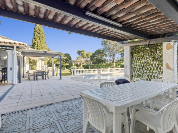Terrace with table and chairs, swimming pool and landscaped garden in the background.