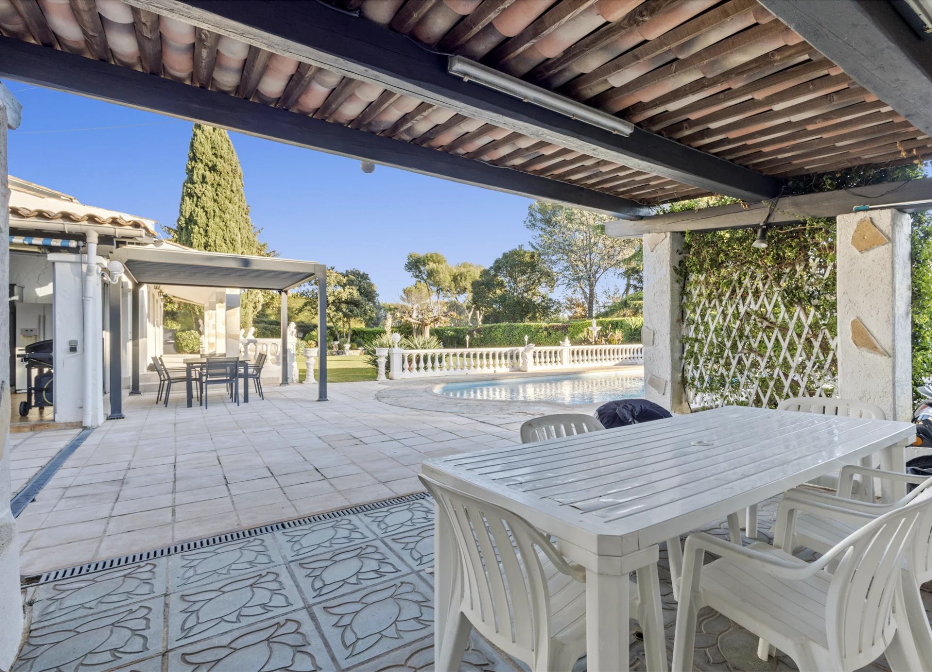 Terrace with table and chairs, swimming pool and landscaped garden in the background.