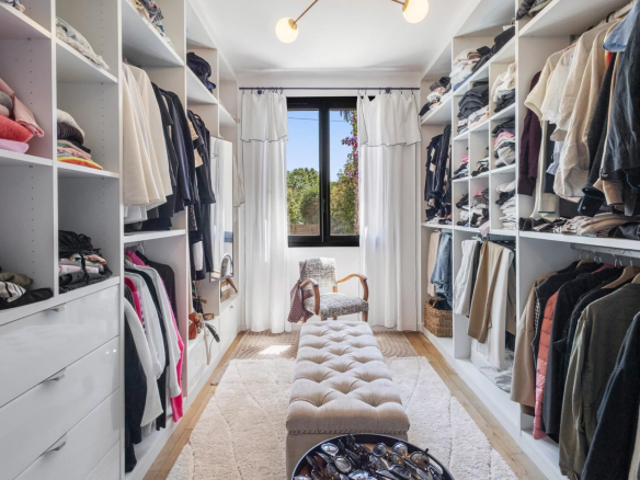 Spacious dressing room with shelves and clothes, window overlooking the outside.