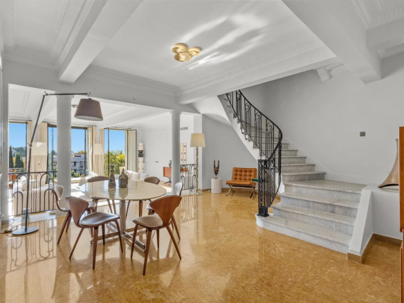 Interior of a renovated private mansion with dining room, staircase and large windows offering a view of the sea.