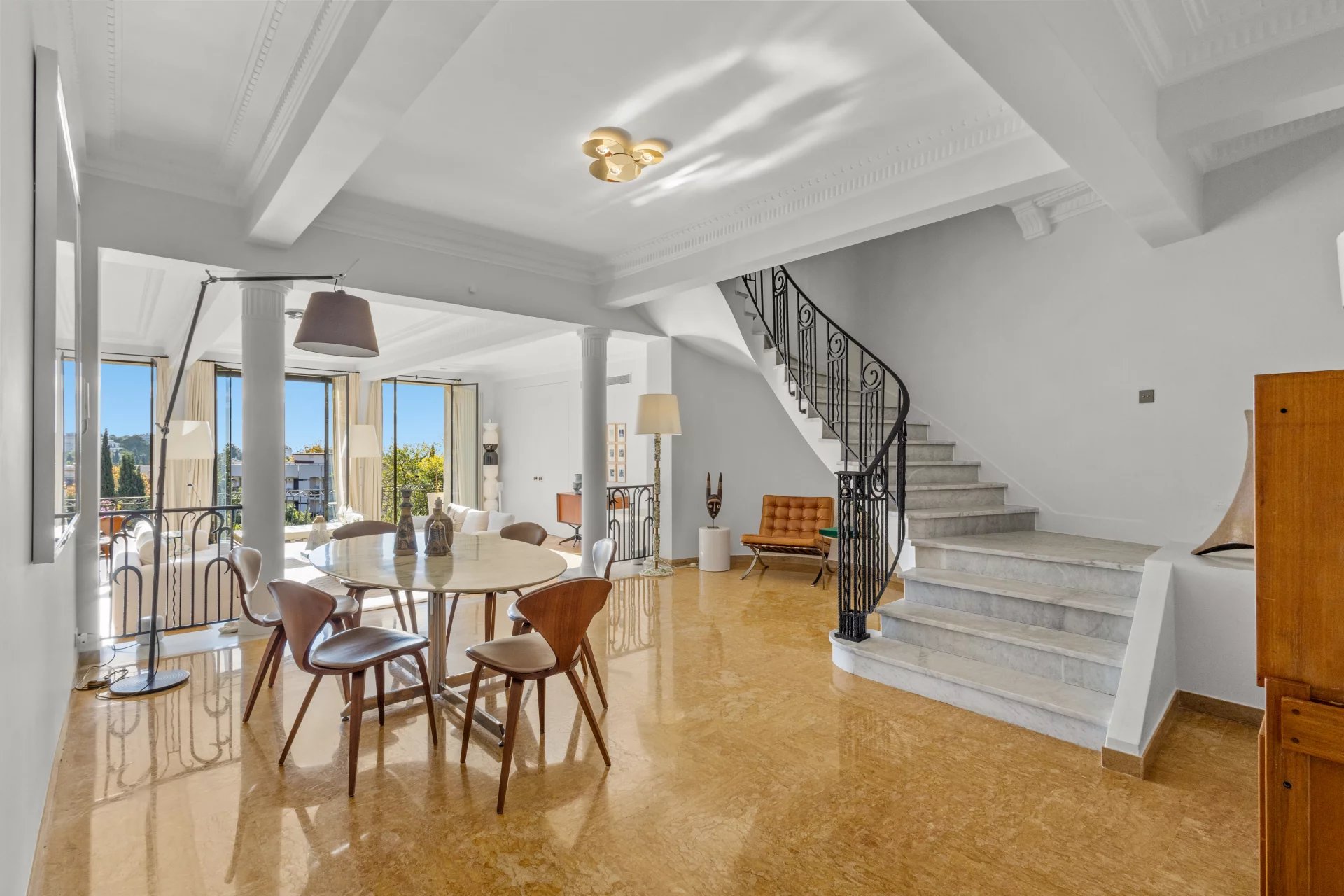 Interior of a renovated private mansion with dining room, staircase and large windows offering a view of the sea.
