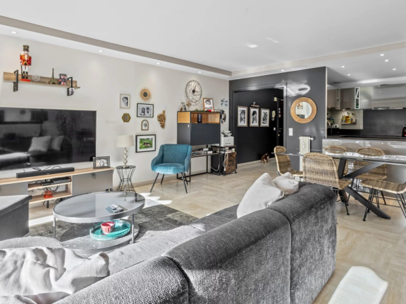 Salon lumineux d'un appartement moderne avec canapé gris, télévision et coin repas.