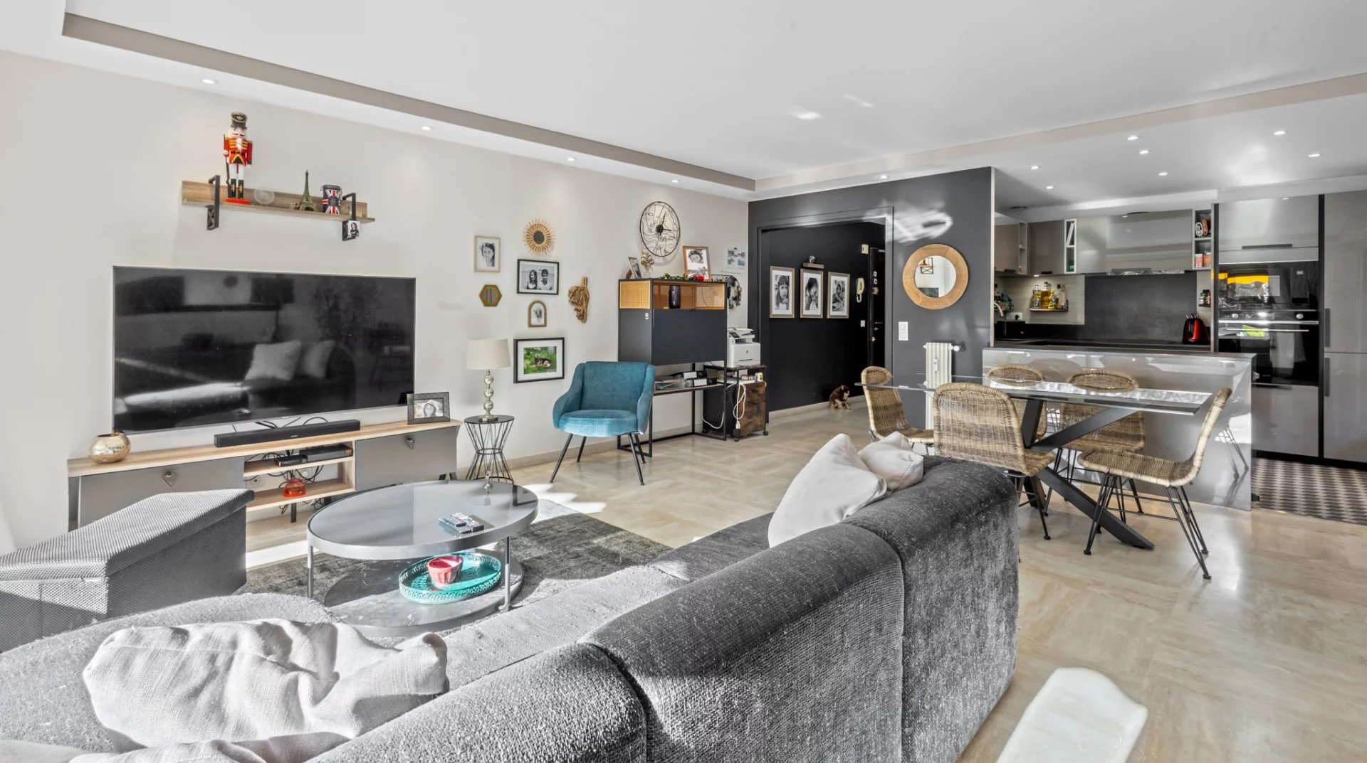 Salon lumineux d'un appartement moderne avec canapé gris, télévision et coin repas.