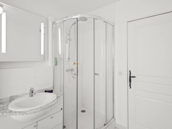 Salle de bain moderne avec douche en verre et lavabo, décorée en blanc et gris.