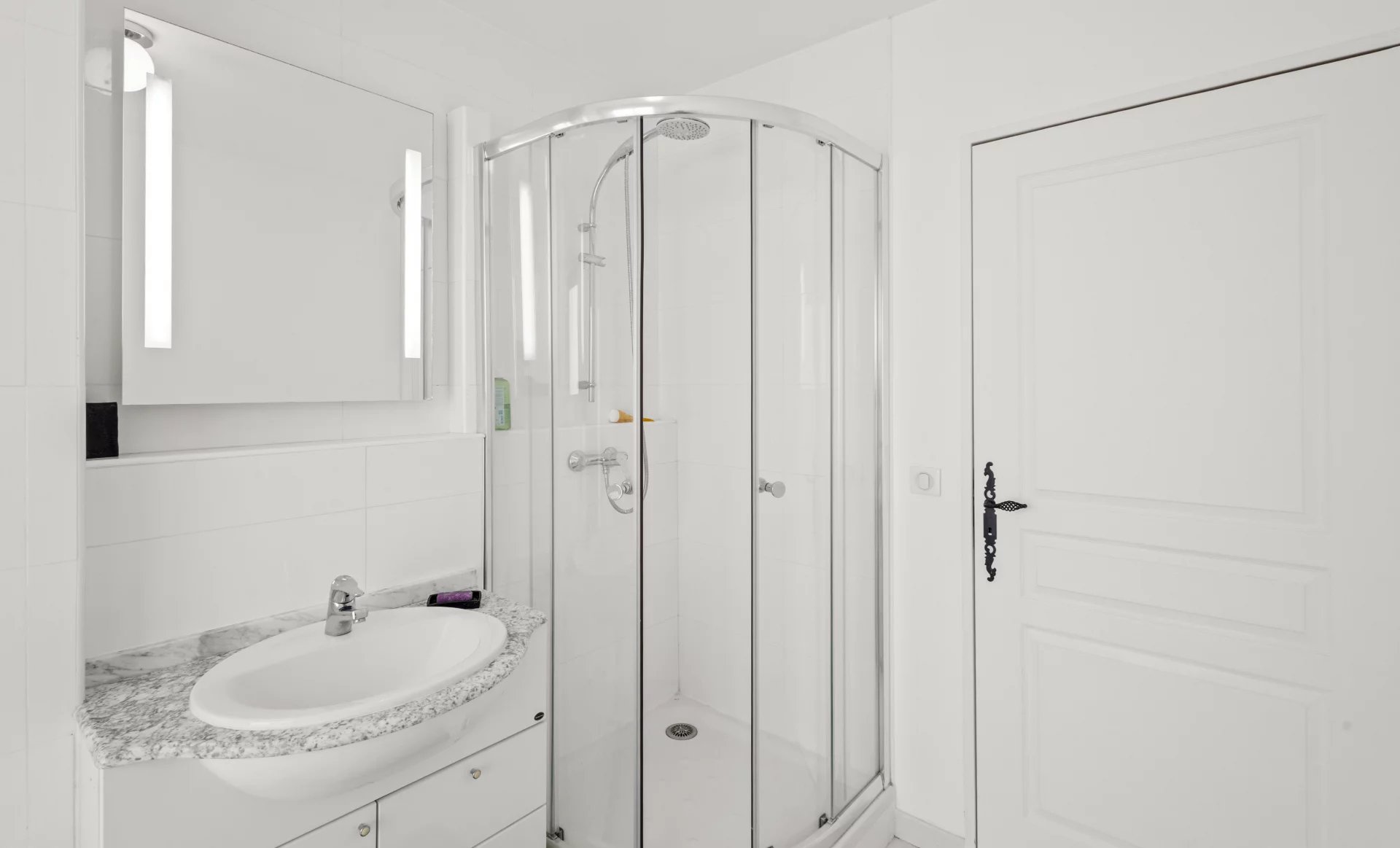 Salle de bain moderne avec douche en verre et lavabo, décorée en blanc et gris.