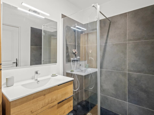 Salle de bain moderne avec douche, meuble en bois et miroir, carrelage gris.