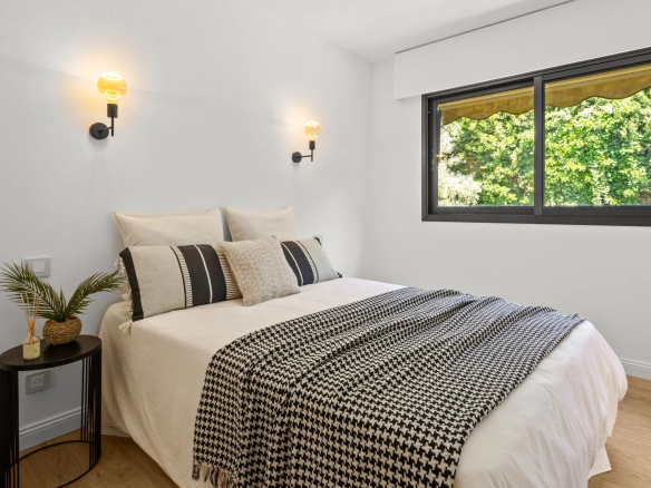 Apartment room with double bed, minimalist decor and window overlooking the outside.