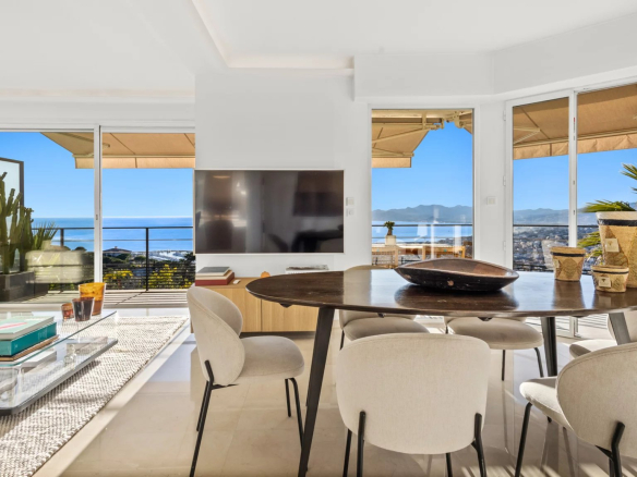 Intérieur d'un appartement moderne avec vue sur la mer, table à manger et salon lumineux.
