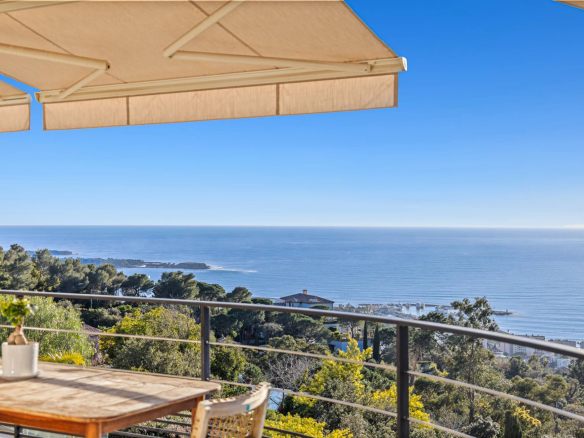 Vue panoramique sur la mer depuis un balcon avec une table en bois et des parasols.